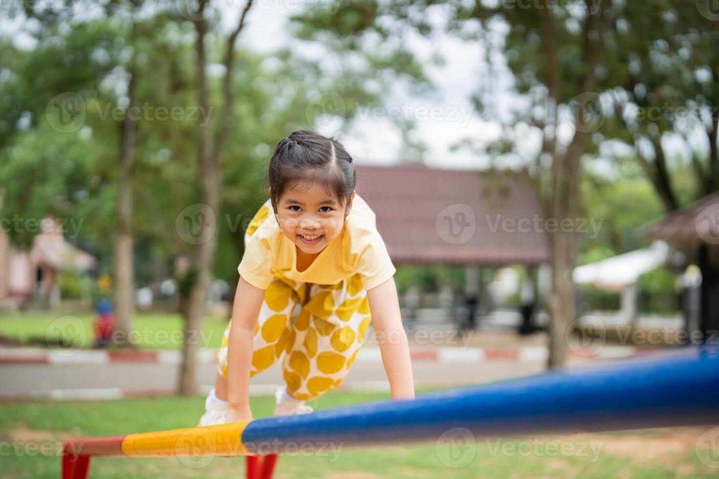 Asian young girl is playing on a playground, climbing on a blue and yellow pole. She is smiling and she is enjoying herself photo