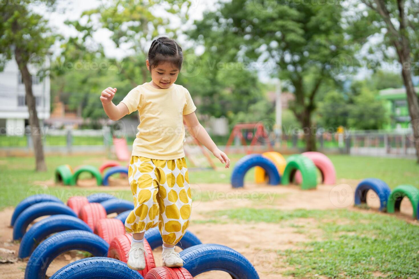Asian young girl is playing in a park with a tire obstacle course. She is wearing a yellow shirt and yellow pants photo