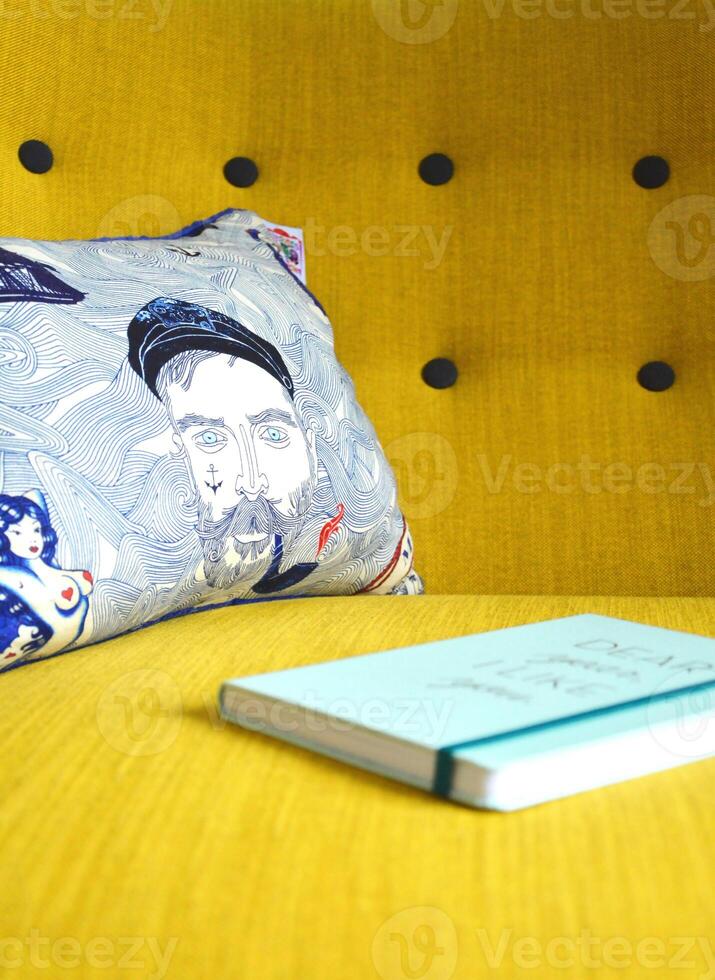 a yellow couch with a pillow and a book photo
