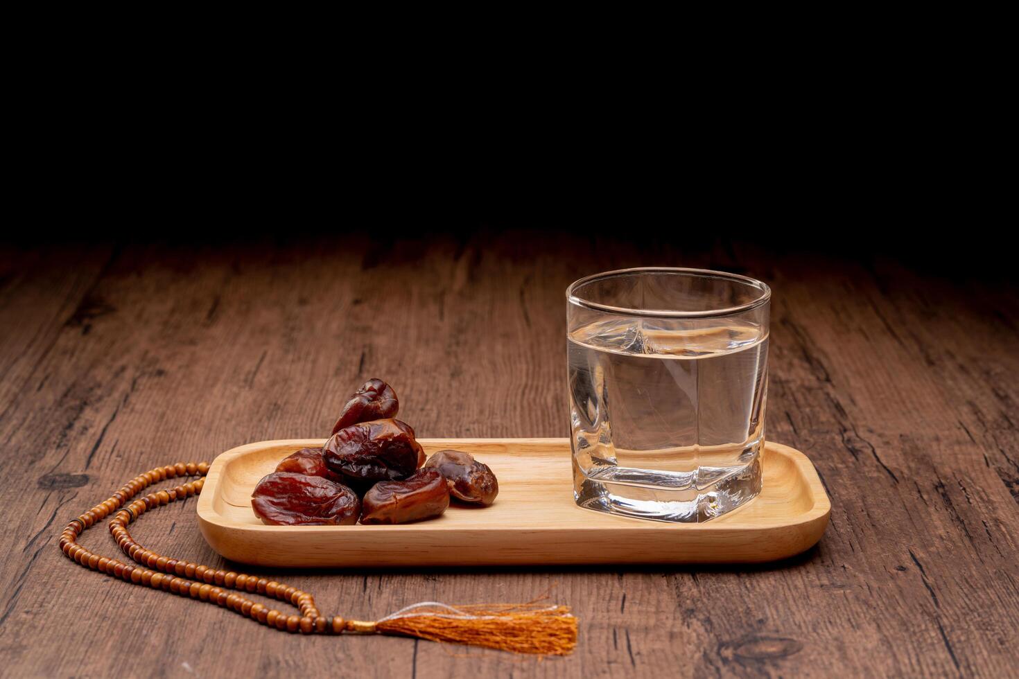 Many Date Palms are on bowls, plates, and cups of water, and the Quran is on wooden tables, to wait for the time of Iftar, with the concept of ramadan Muslims, Arabic calligraphy meaning of Al Quran photo