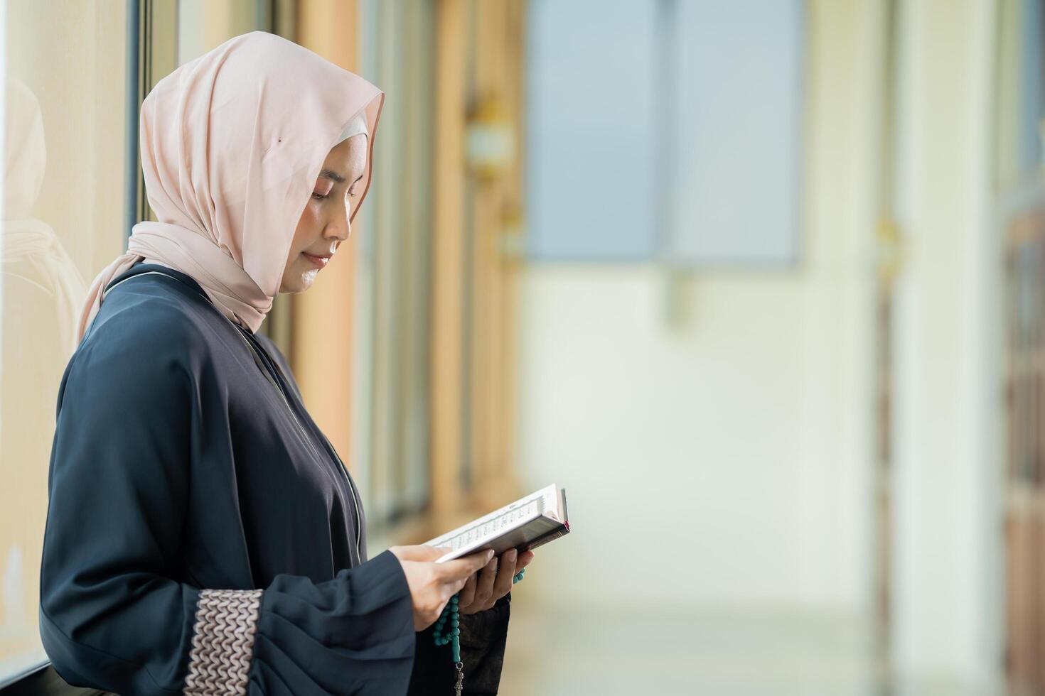 The image of an Asian Muslim woman in the Islamic religion in hijab in cream color. reading the Quran and having a happy smiling face Staying in a beautiful mosque out of respect for God. photo