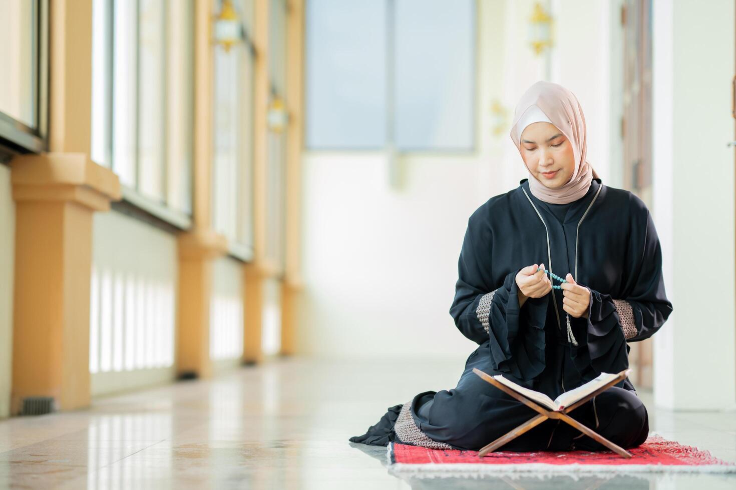 The image of an Asian Muslim woman in the Islamic religion in hijab in cream color. reading the Quran and having a happy smiling face Staying in a beautiful mosque out of respect for God. photo