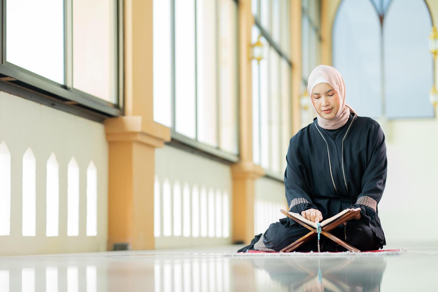 The image of an Asian Muslim woman in the Islamic religion in hijab in cream color. reading the Quran and having a happy smiling face Staying in a beautiful mosque out of respect for God. photo