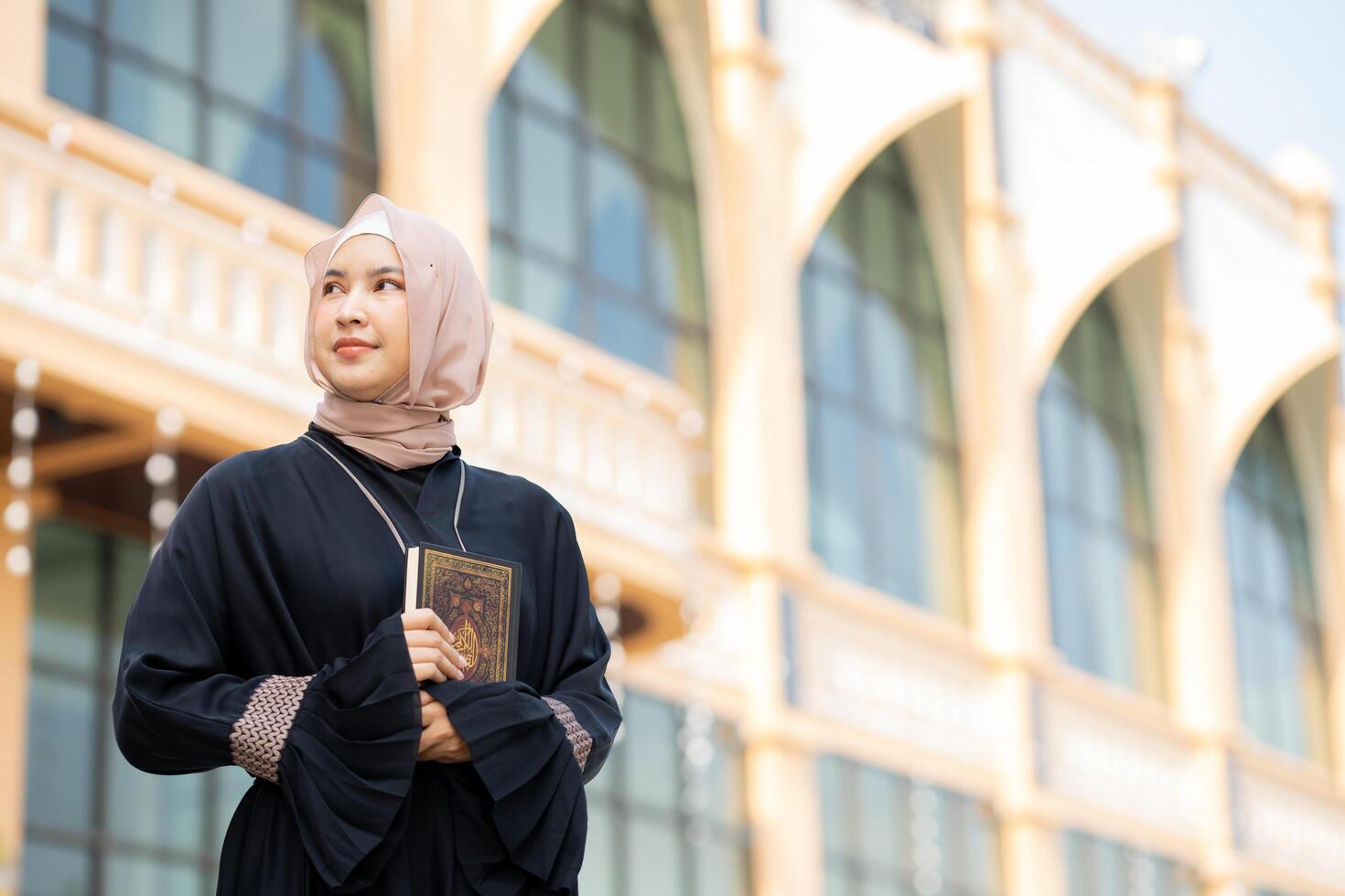 The image of an Asian Muslim woman in the Islamic religion in hijab in cream color. reading the Quran and having a happy smiling face Staying in a beautiful mosque out of respect for God. photo