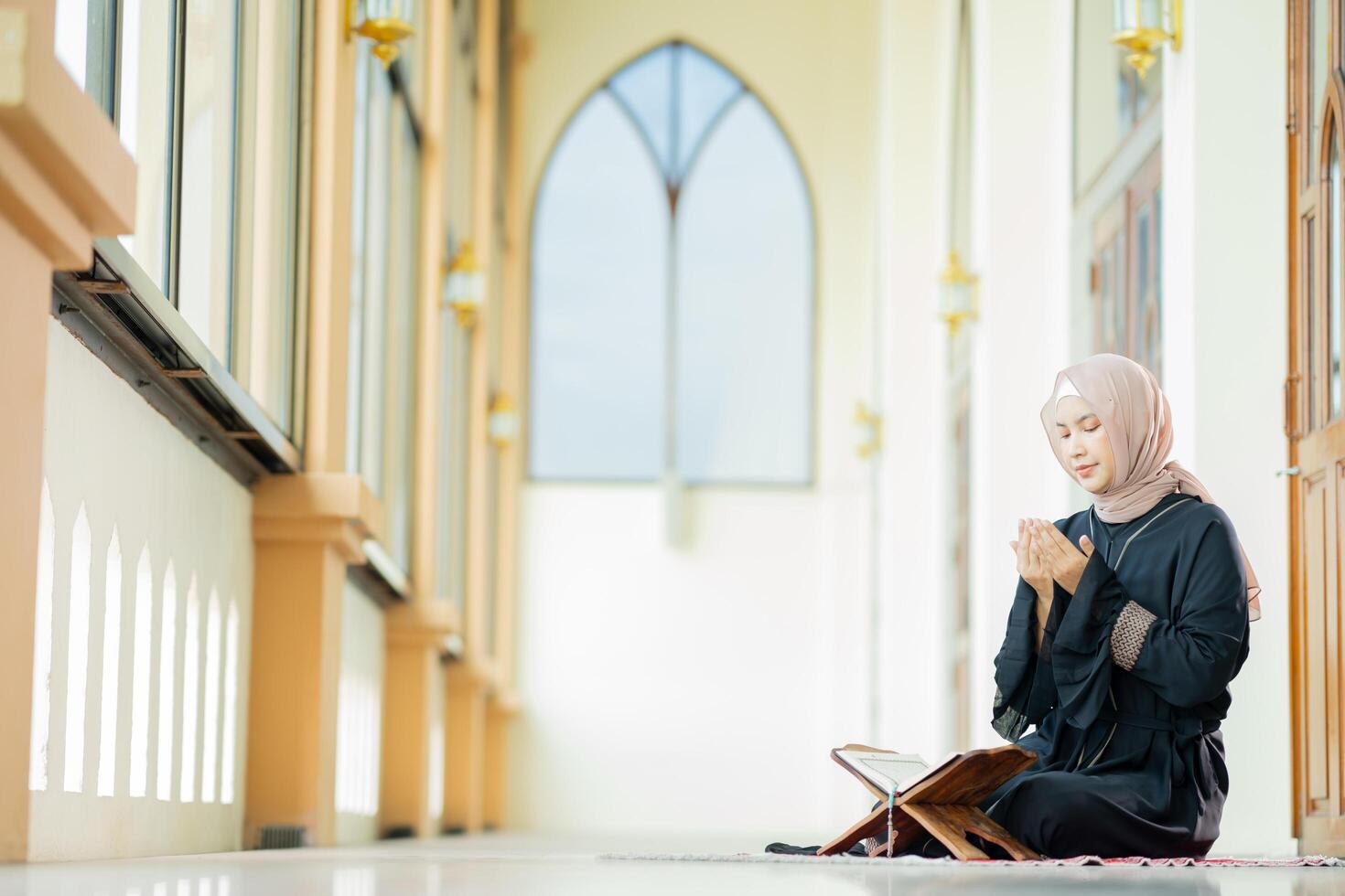 The image of an Asian Muslim woman in the Islamic religion in hijab in cream color. reading the Quran and having a happy smiling face Staying in a beautiful mosque out of respect for God. photo