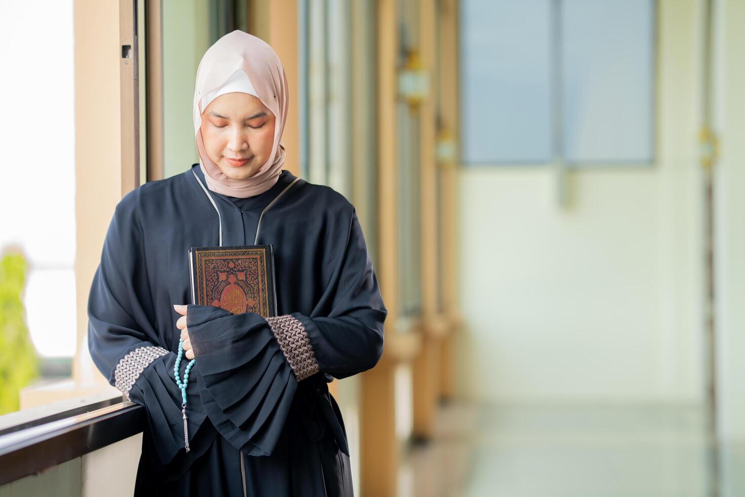 The image of an Asian Muslim woman in the Islamic religion in hijab in cream color. reading the Quran and having a happy smiling face Staying in a beautiful mosque out of respect for God. photo