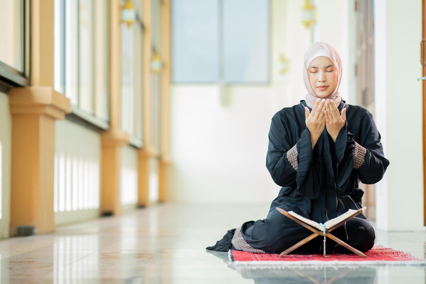 The image of an Asian Muslim woman in the Islamic religion in hijab in cream color. reading the Quran and having a happy smiling face Staying in a beautiful mosque out of respect for God. photo