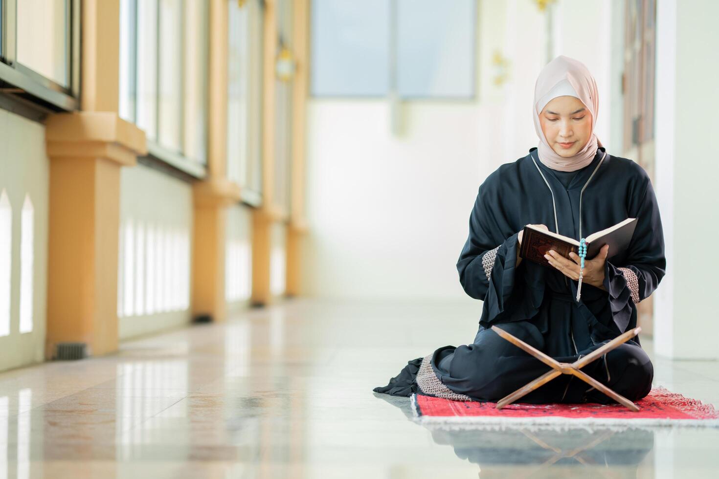 The image of an Asian Muslim woman in the Islamic religion in hijab in cream color. reading the Quran and having a happy smiling face Staying in a beautiful mosque out of respect for God. photo