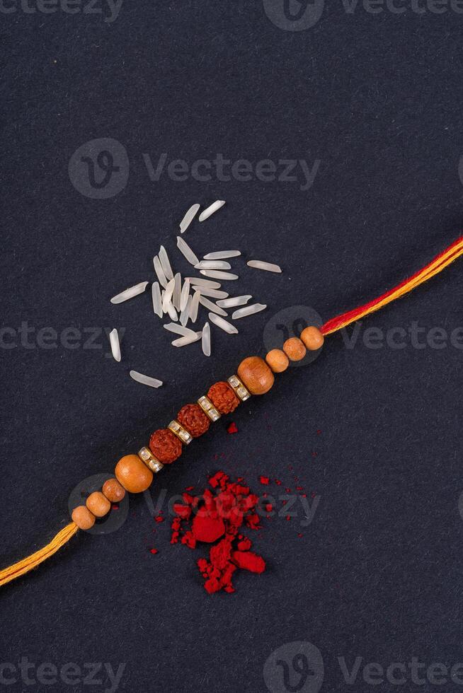 Raksha Bandhan Rakhi with rice grains and kumkum on black background, Traditional Indian wrist band which is a symbol of love between Brothers and Sisters. photo