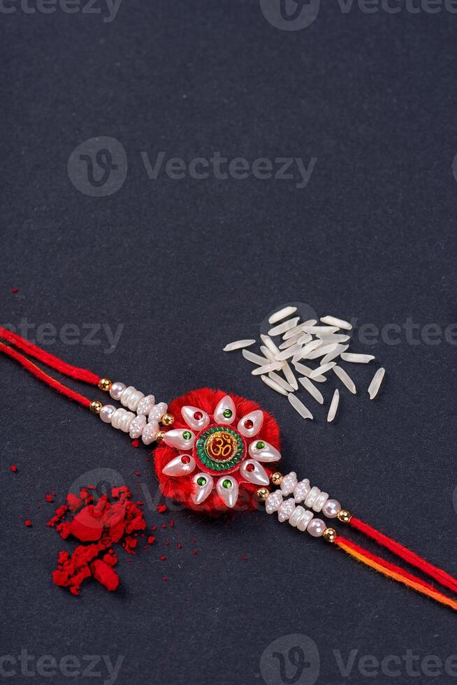 Raksha Bandhan Rakhi with rice grains and kumkum on black background, Traditional Indian wrist band which is a symbol of love between Brothers and Sisters. photo