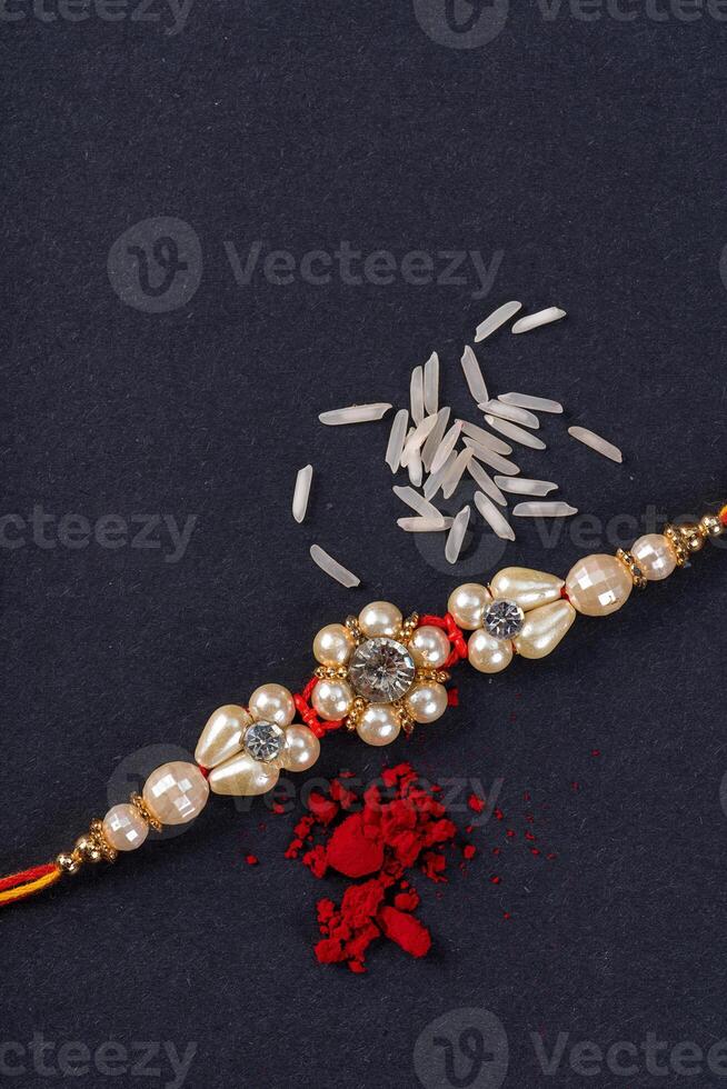 Raksha Bandhan Rakhi with rice grains and kumkum on black background, Traditional Indian wrist band which is a symbol of love between Brothers and Sisters. photo