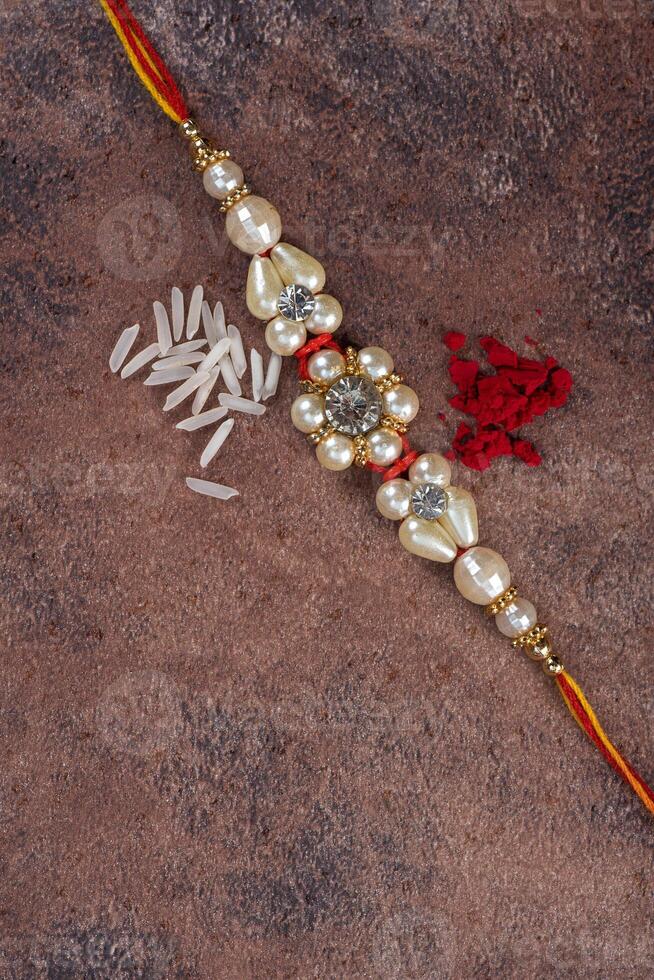 Raksha Bandhan Rakhi with rice grains and kumkum on stone background, Traditional Indian wrist band which is a symbol of love between Brothers and Sisters. photo