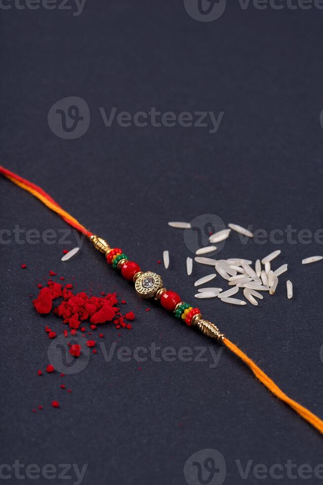 Raksha Bandhan Rakhi with rice grains and kumkum on black background, Traditional Indian wrist band which is a symbol of love between Brothers and Sisters. photo