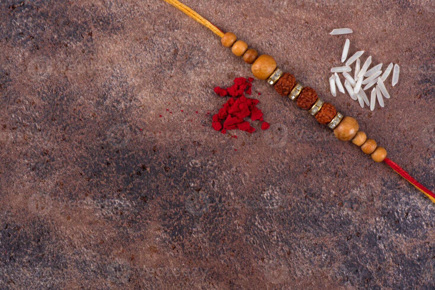 Raksha Bandhan Rakhi with rice grains and kumkum on stone background, Traditional Indian wrist band which is a symbol of love between Brothers and Sisters. photo