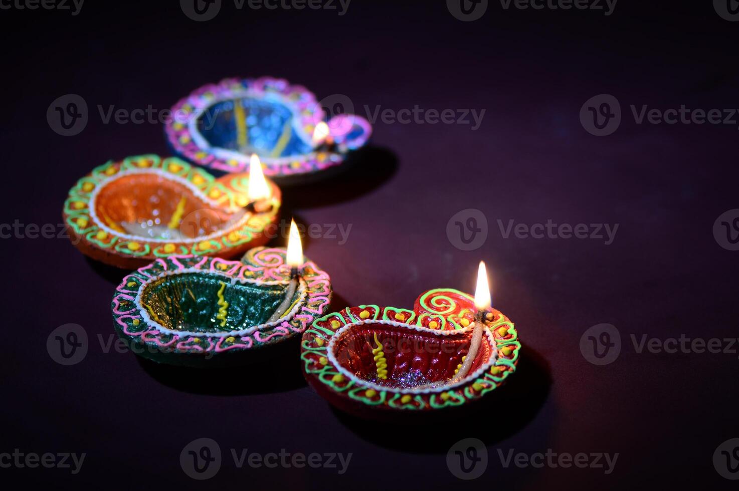 Three colorful diyas lit with candles on a dark surface photo