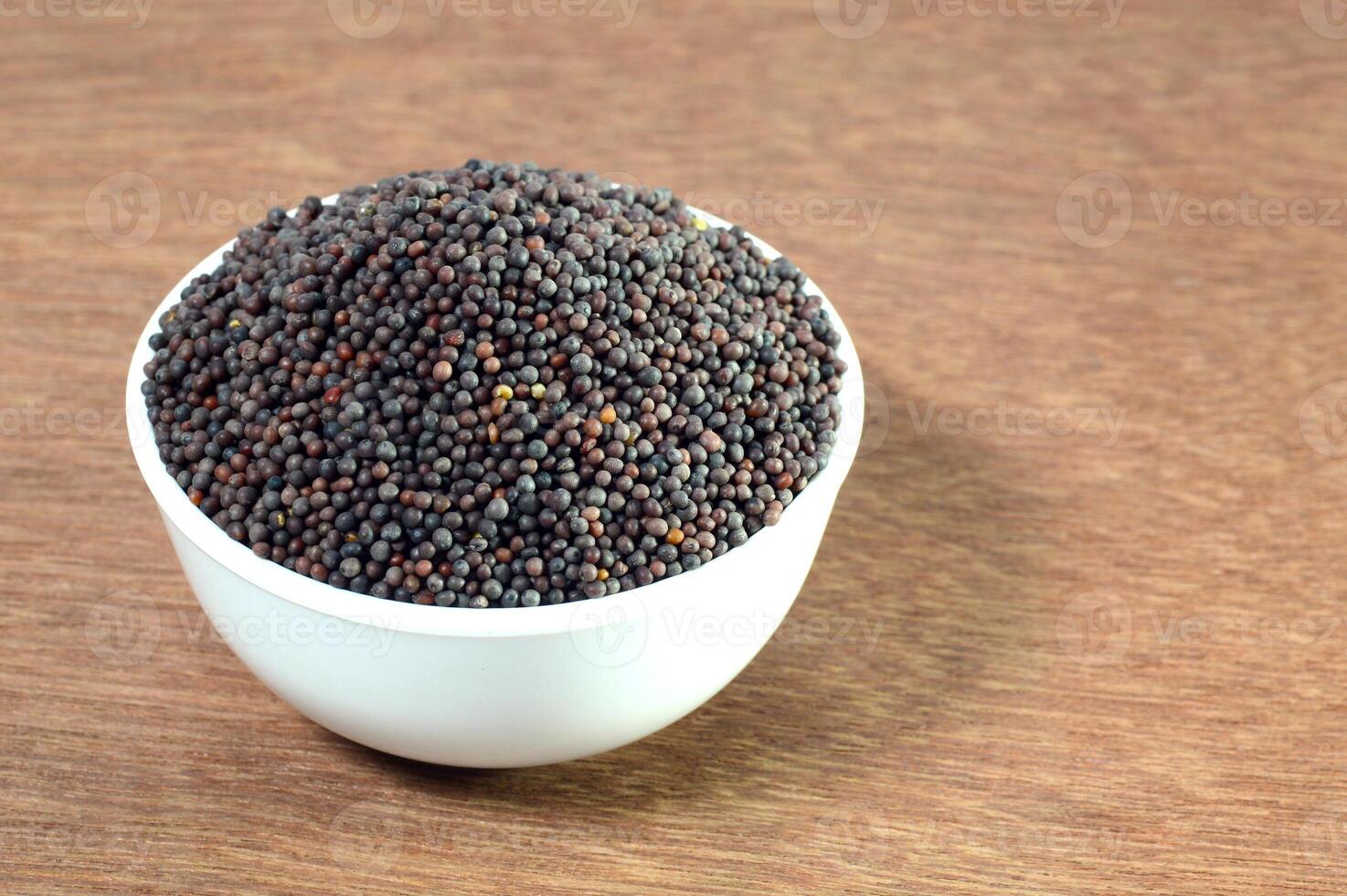 A bowl of black mustard seeds on a wooden table photo
