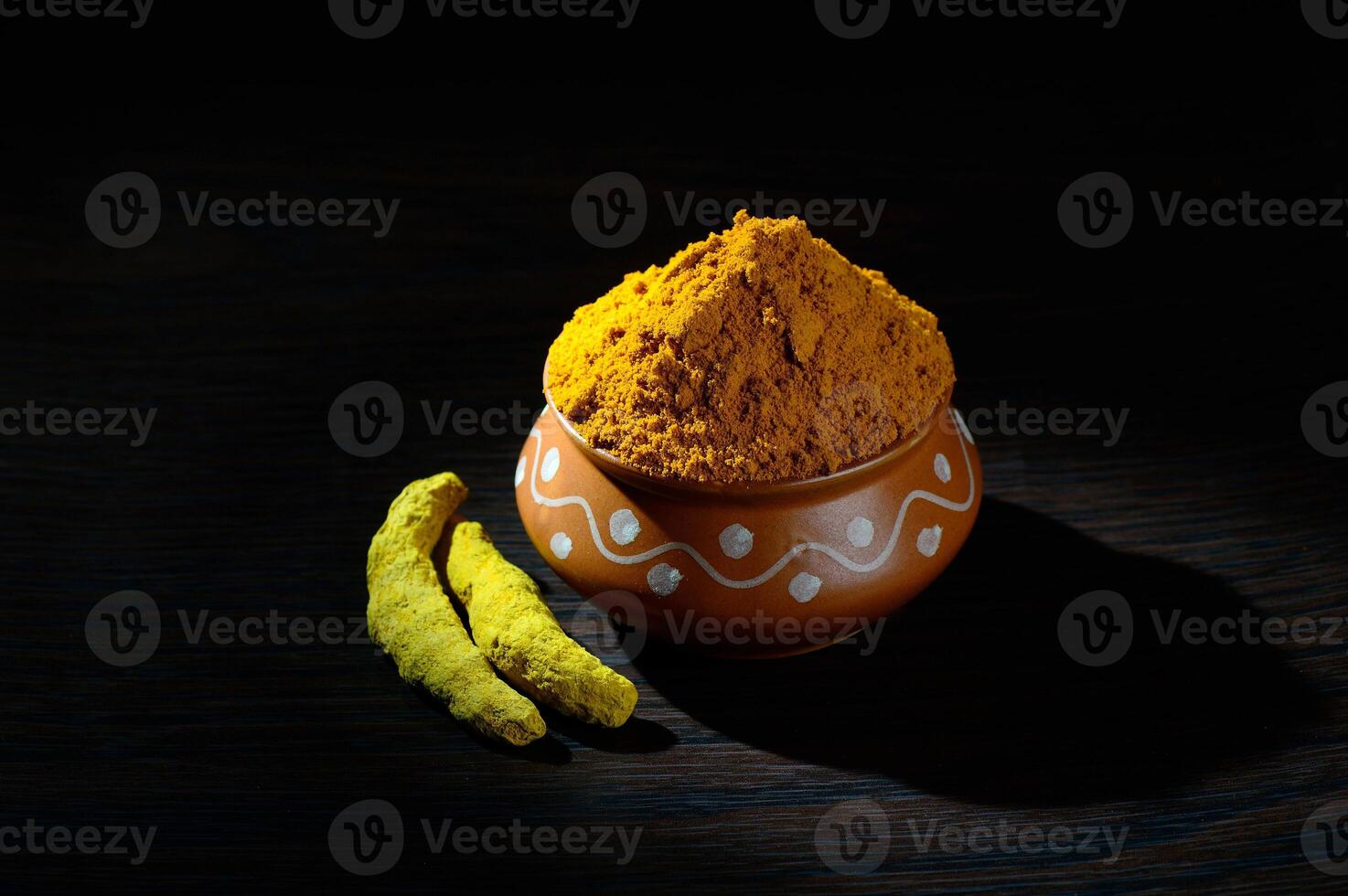 Turmeric powder in clay pot with roots or barks on black background photo