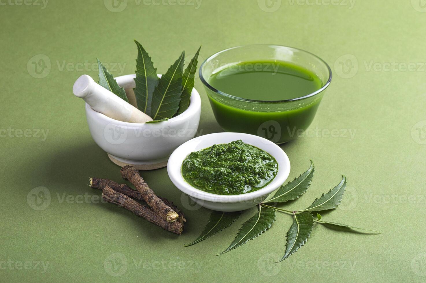 Medicinal Neem leaves in mortar and pestle with neem paste, juice and twigs on green background photo