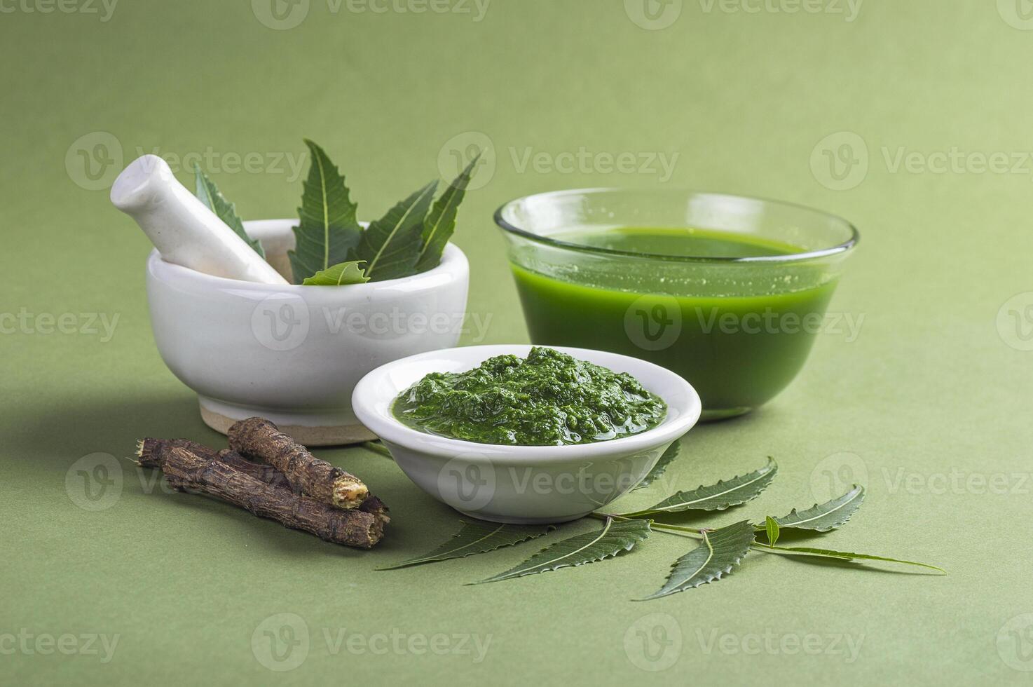 Medicinal Neem leaves in mortar and pestle with neem paste, juice and twigs on green background photo