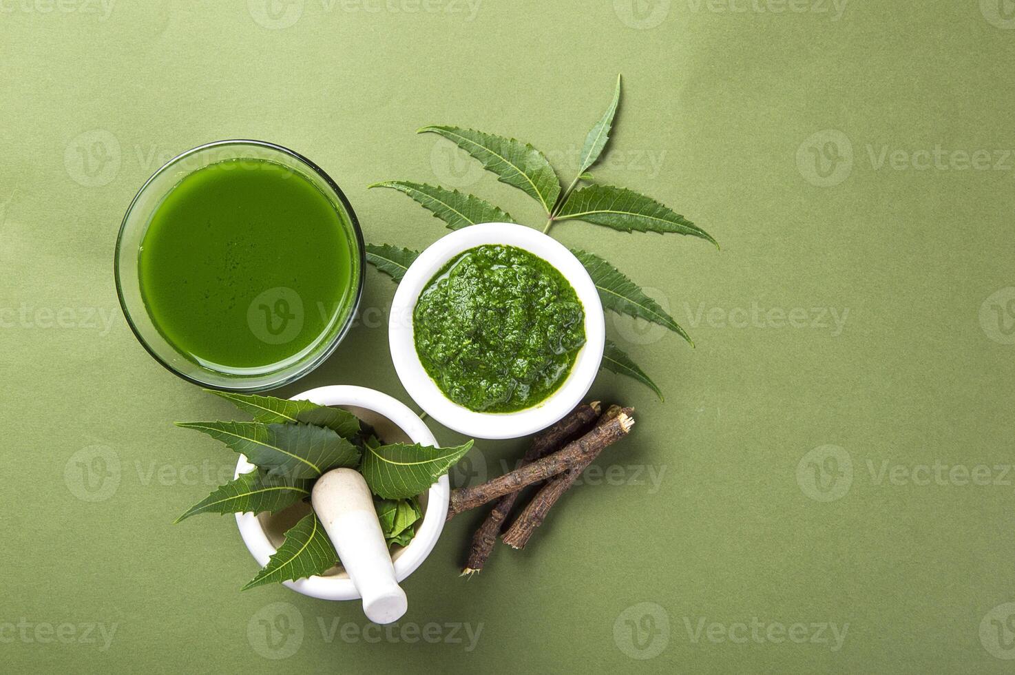 Medicinal Neem leaves in mortar and pestle with neem paste, juice and twigs on green background photo