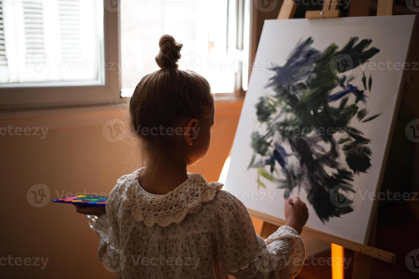 little cute girl draws with paints on canvas at the easel photo