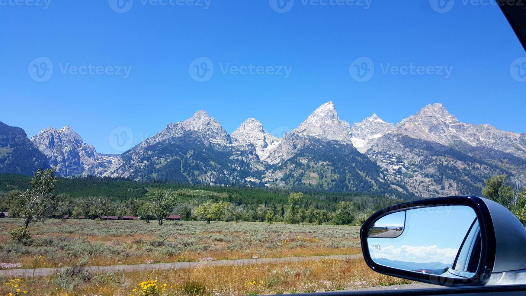 View of Mountains and Rear View Mirror of Car, Driving on Summer Road Trip photo