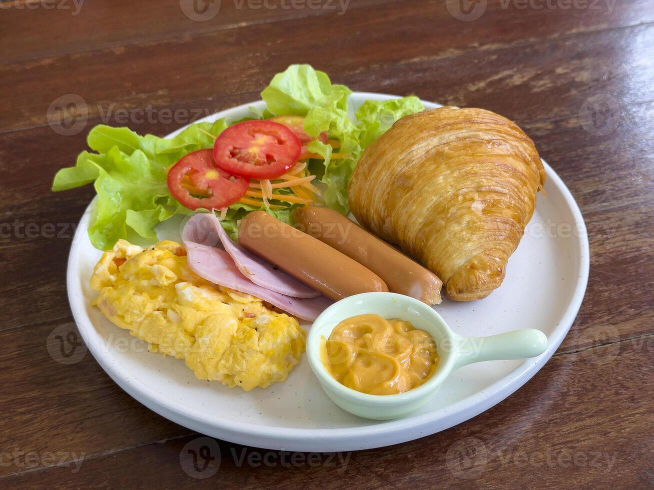 Croissants with stuffing in a plate on a wooden dining table. croissant with chicken sausage, ham, omelet and vegetables,tomato . The concept of breakfast, fast food, snack. side view photo