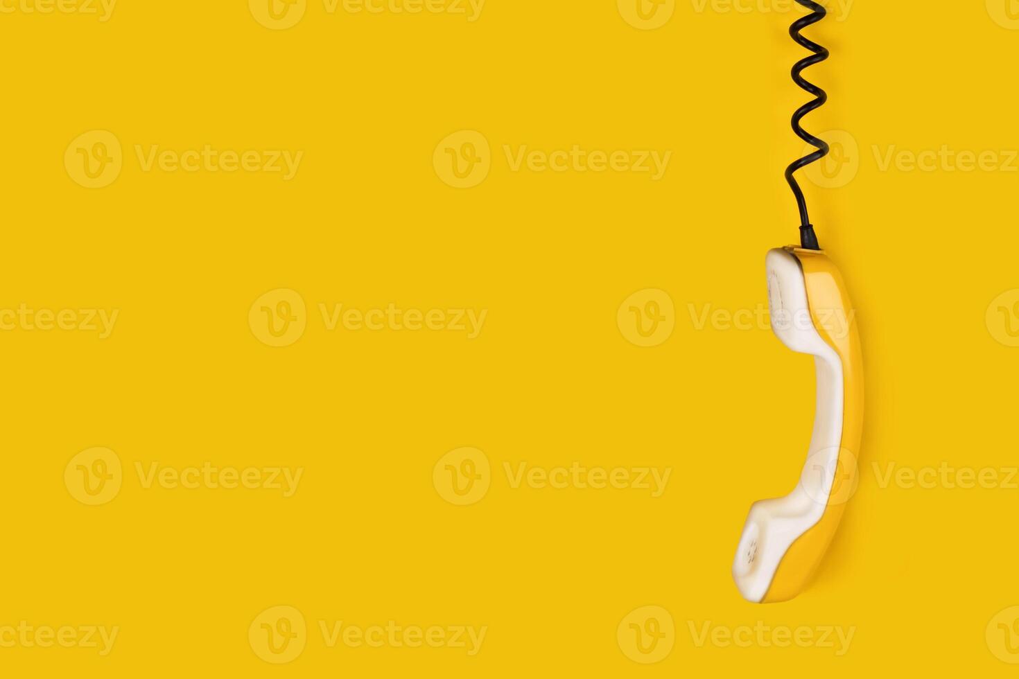 Yellow old phone handset dangles on wire. yellow background banner poster copy space photo