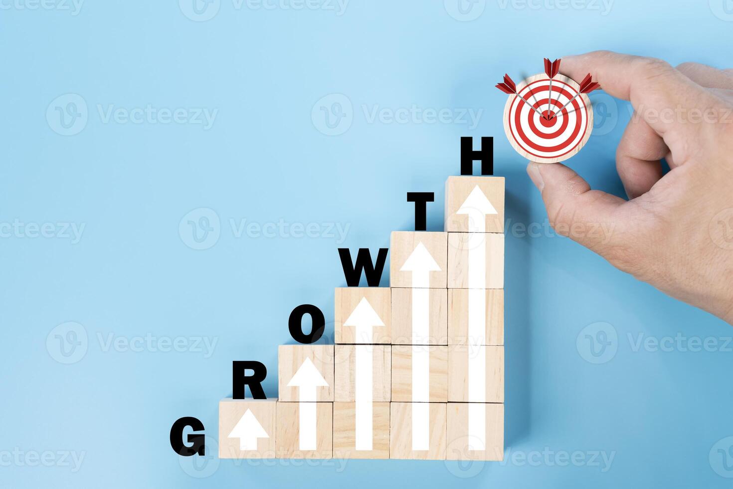 Hand holding wooden block with target aiming dart board and arrow up on blue background. photo