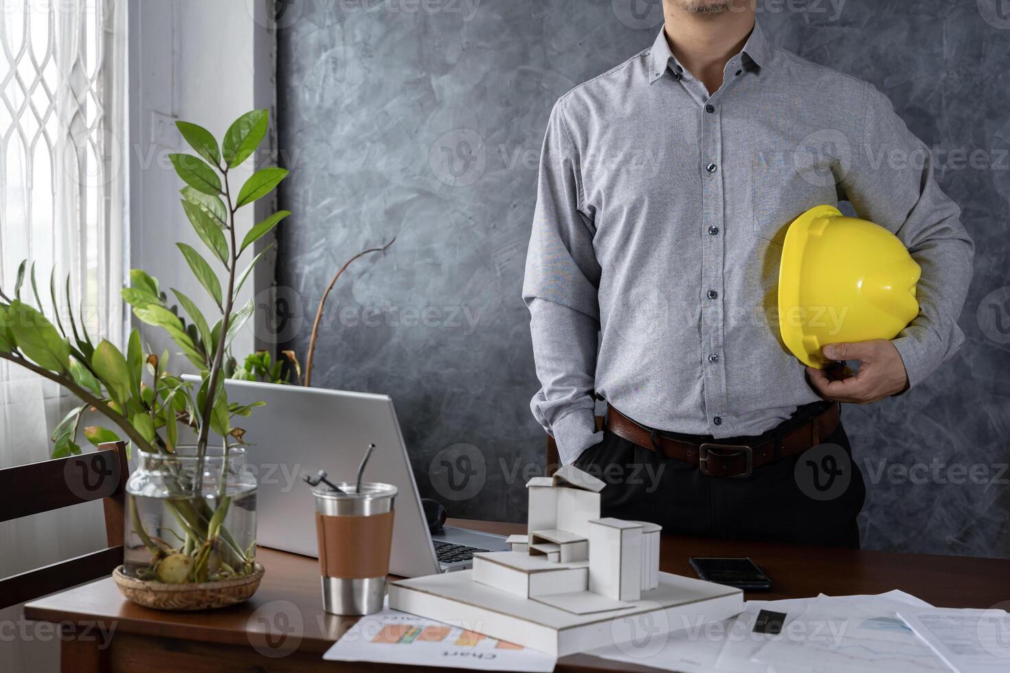 Engineer holding helmet checking accuracy of building structural blueprints from architect on the desk in office to proceed with the construction. photo