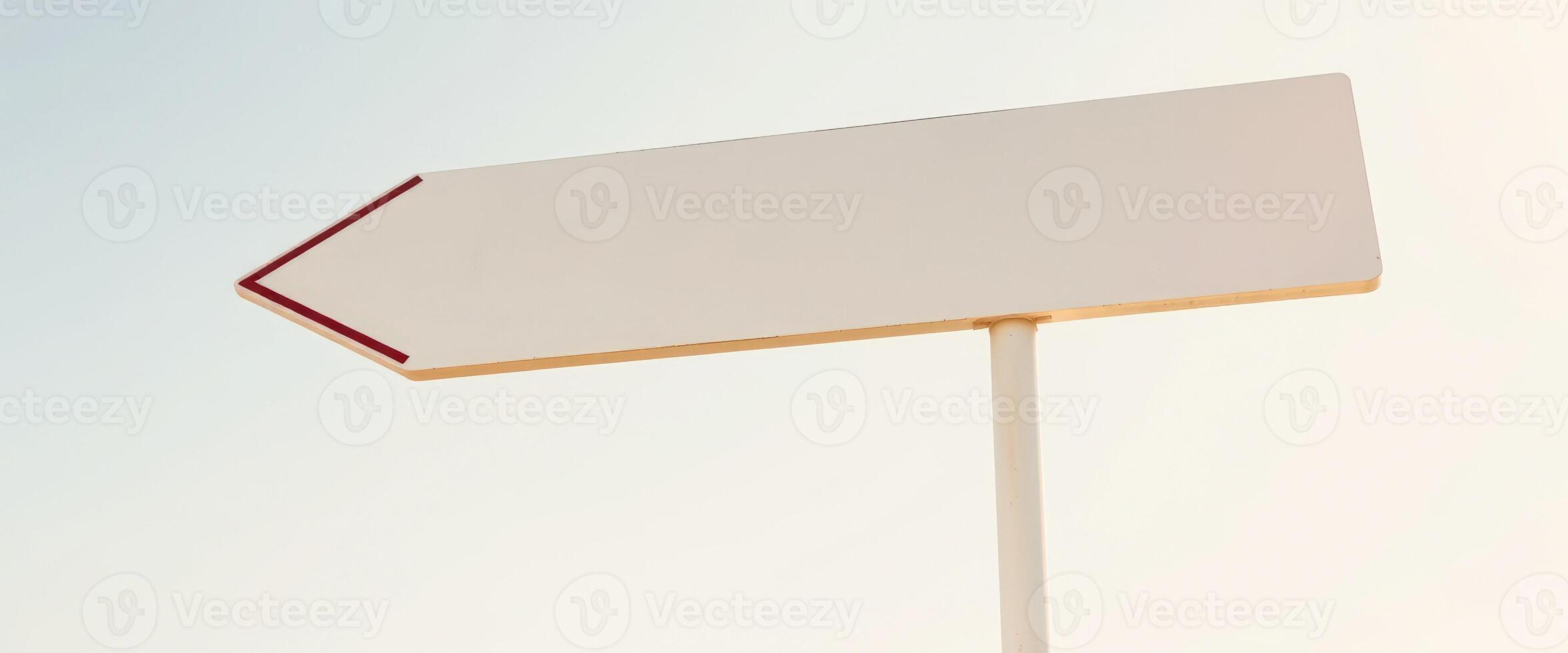 white arrow sign points left against a light blue sky photo