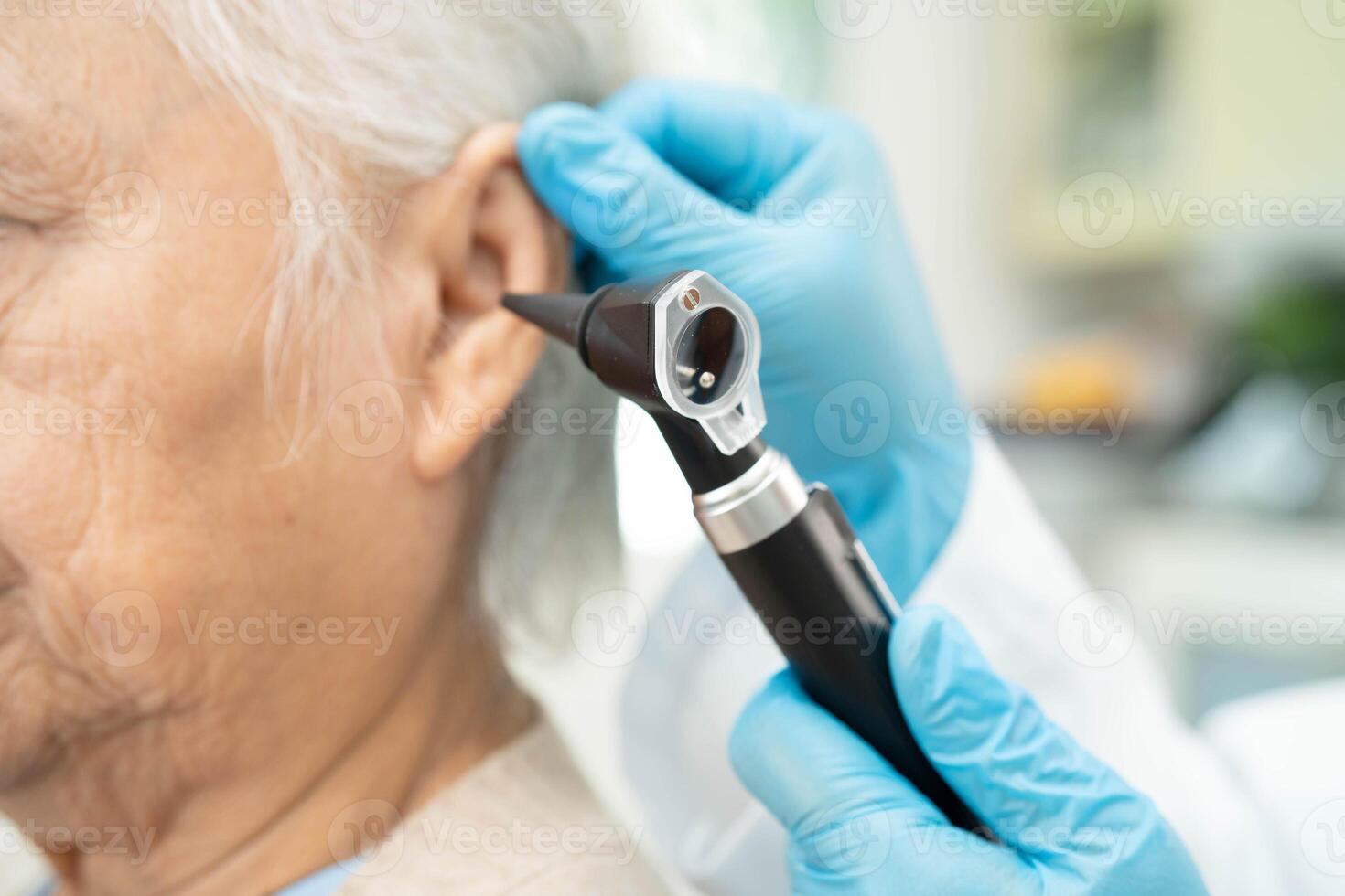 Otolaryngologist or ENT physician doctor examining senior patient ear with otoscope, hearing loss problem. photo