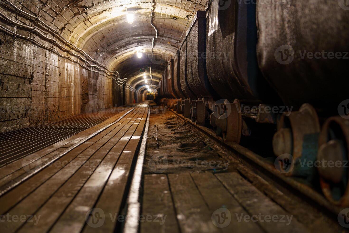 This image depicts a rusty, dark mine tunnel with wooden tracks and metal mining carts, illuminated by a few dim lights, showcasing the essence of underground industrial exploration, gold mine photo