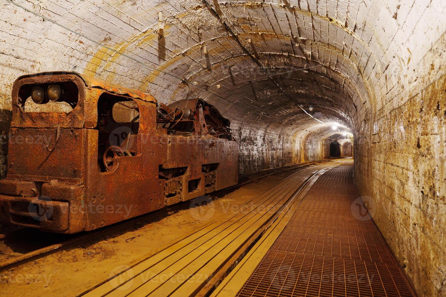 An old rusty mining train sits abandoned in a dark tunnel. The tracks lead into the shadows, creating a mysterious atmosphere, ideal for stories about mining and industry. photo