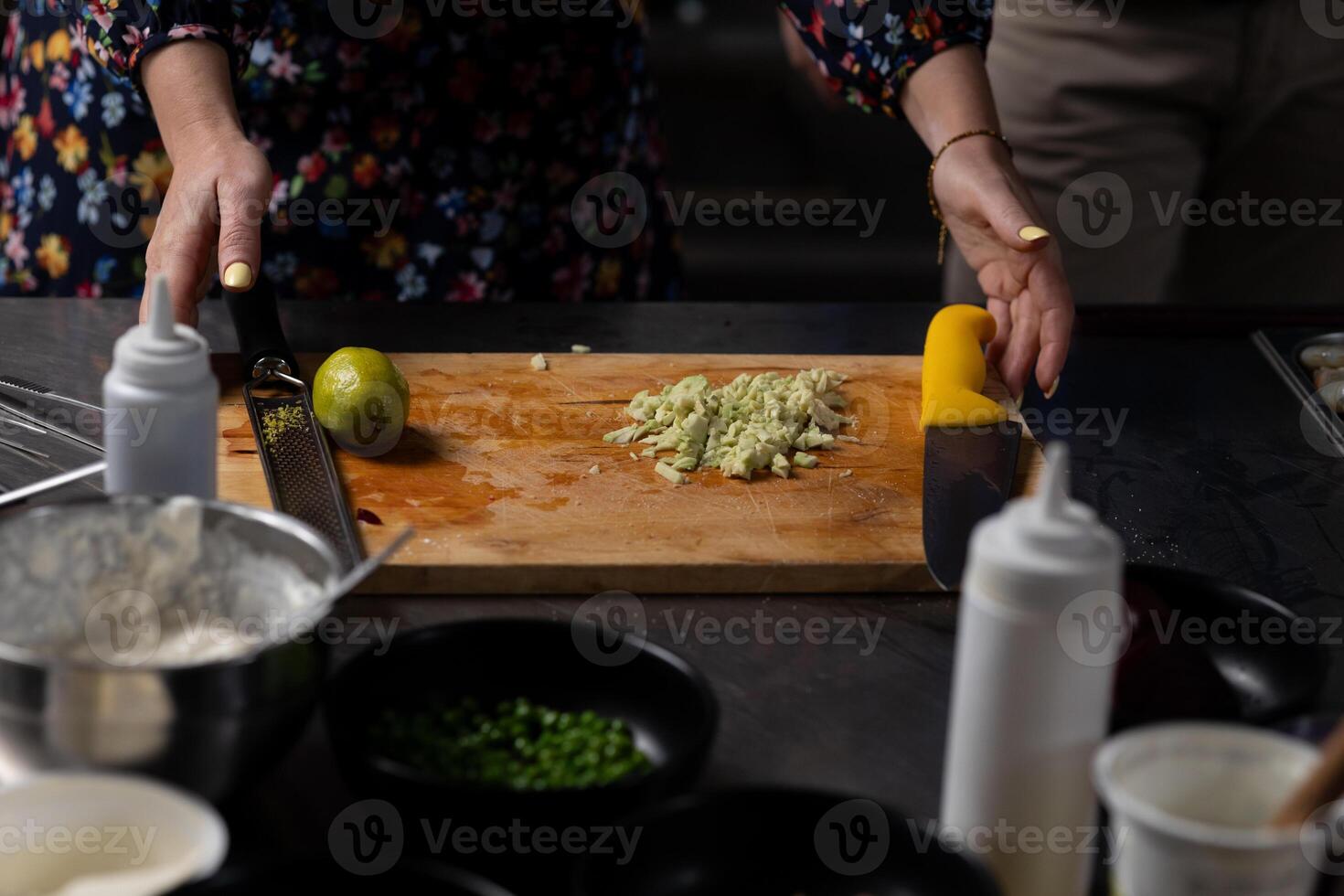 Hands of woman chopping fresh avocado on wooden board, with lime beside it. Various ingredients are ready for preparation photo