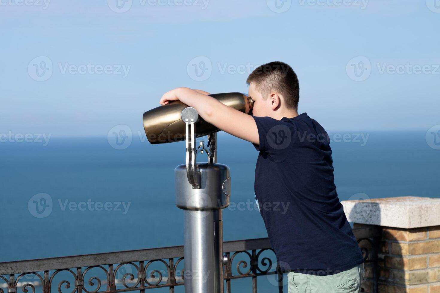 Teenager boy looking in binoculars telescope on observation deck for tourist. Travel, tourism, outdoors lifestyle holiday vacation. Side view photo