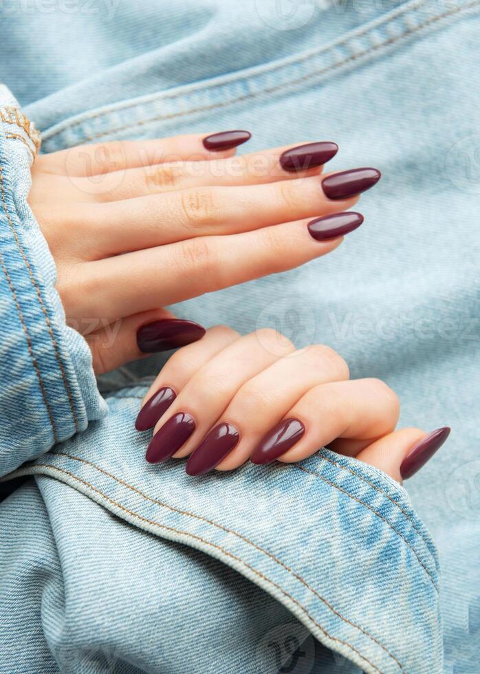 A close-up of elegantly manicured hands showcasing deep burgundy nail polish against a casual denim background photo