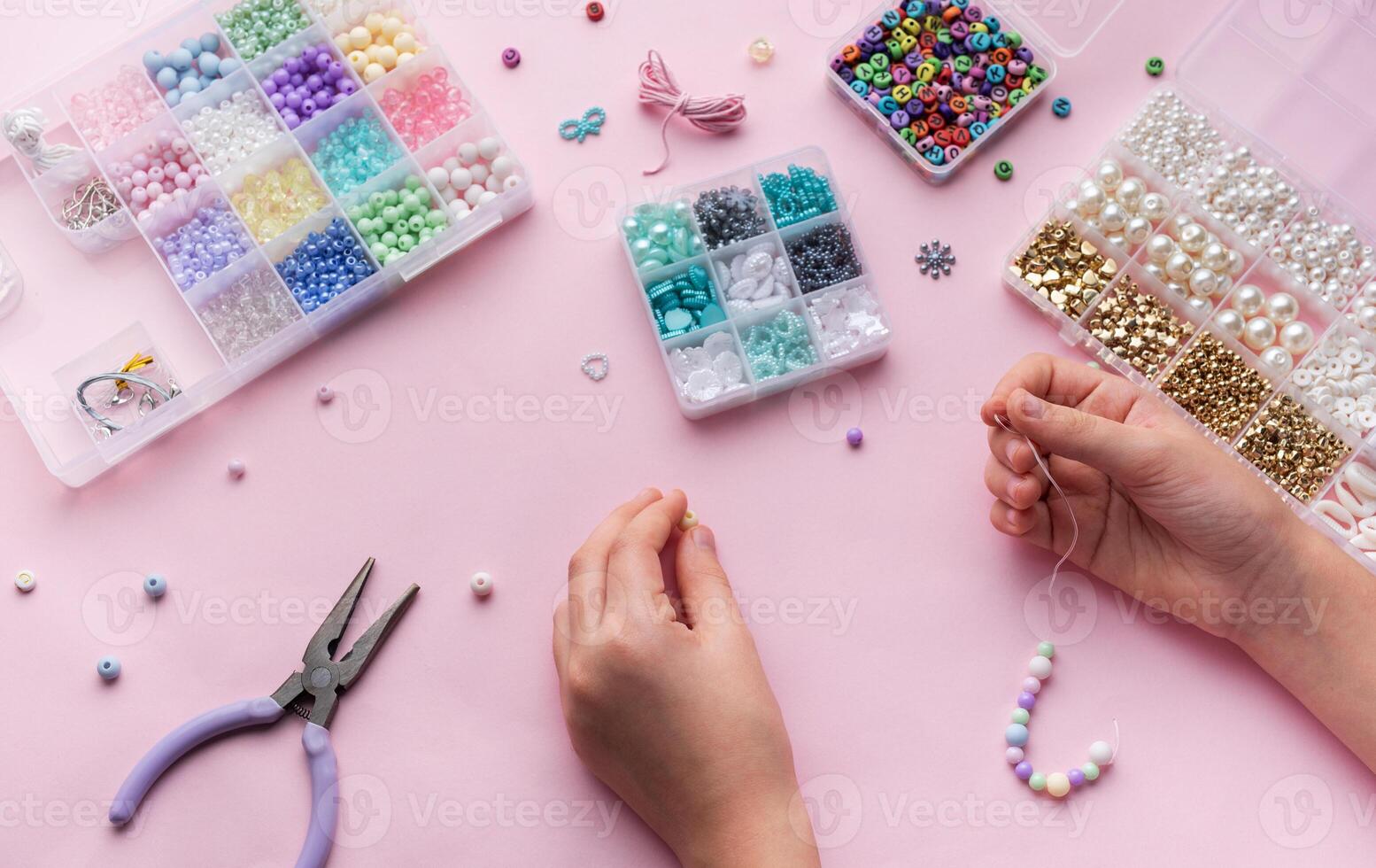 Creating colorful beaded jewelry with assorted beads and crafting tools on a light pink surface photo