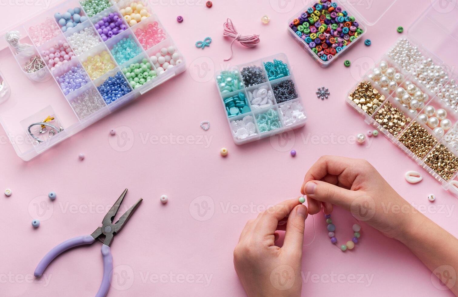 Creating colorful beaded jewelry with assorted beads and crafting tools on a light pink surface photo