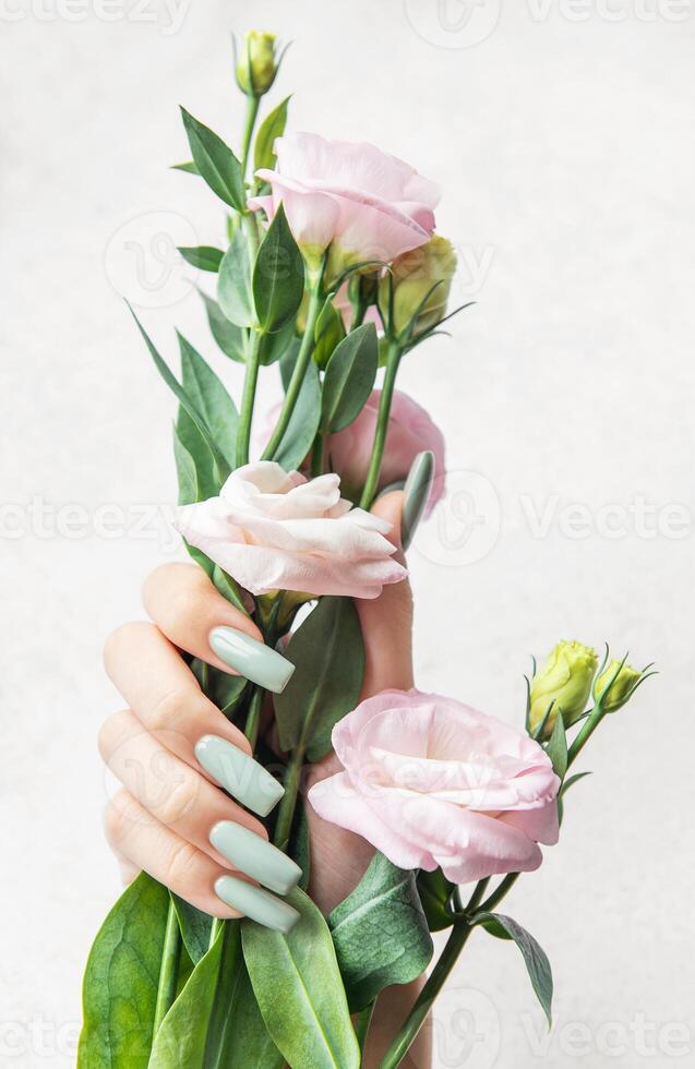 Delicate hand holding a bouquet of pale pink flowers against a soft background in natural light photo