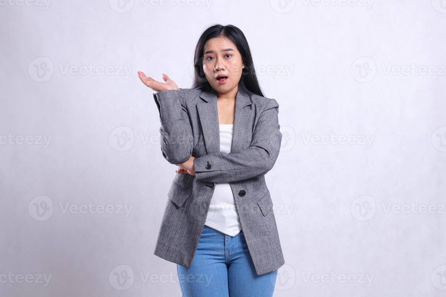 expression of young beautiful woman surprised arms crossed offering to right wearing grey jacket and jeans standing isolated on white background. for advertising content, fashion, banner, magazine photo
