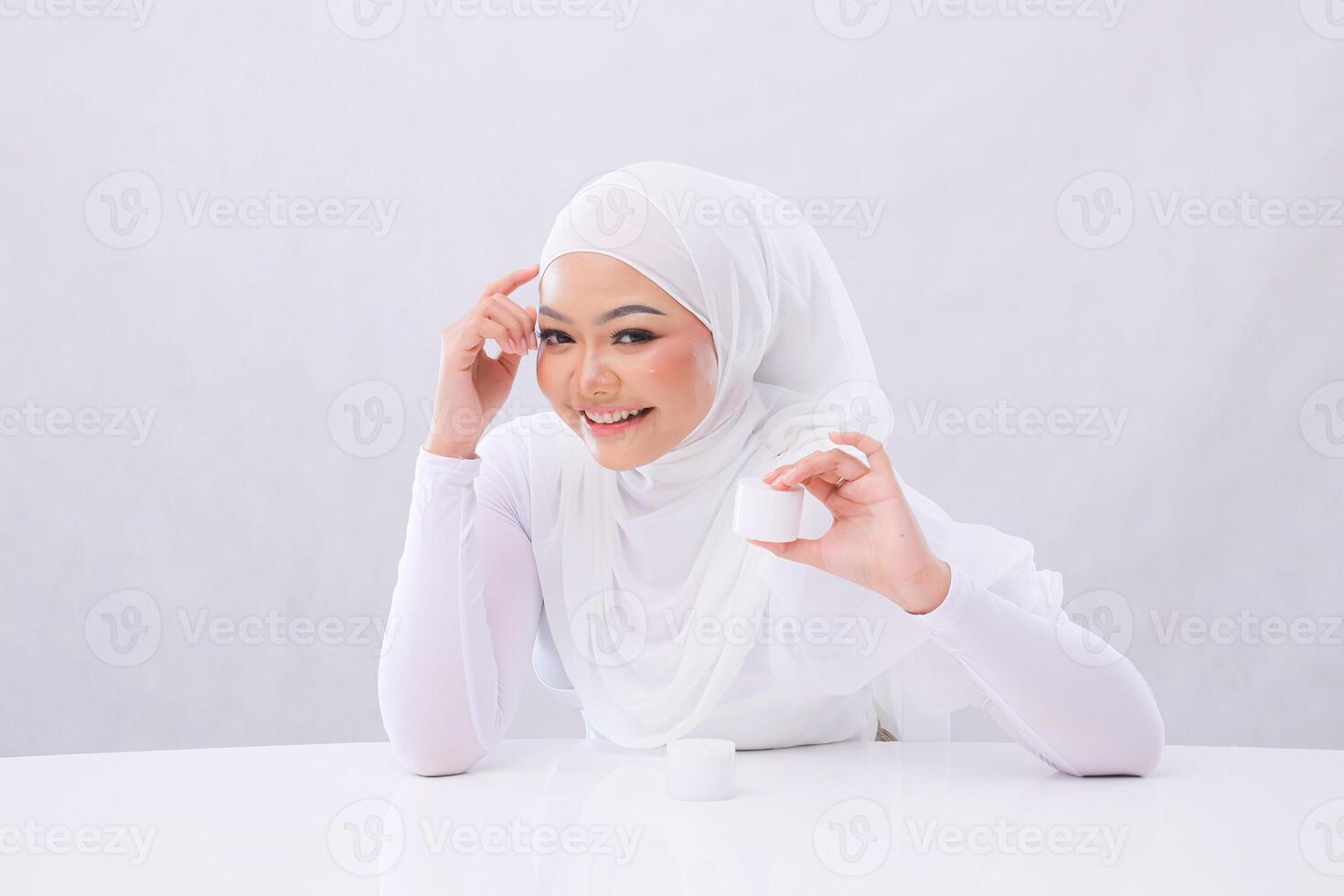 Charm Beautiful young girl laughing relaxed look in front of hand sticking hijab and holding cosmetic cream in front of head to display skin care products with white background. health,medical concept photo