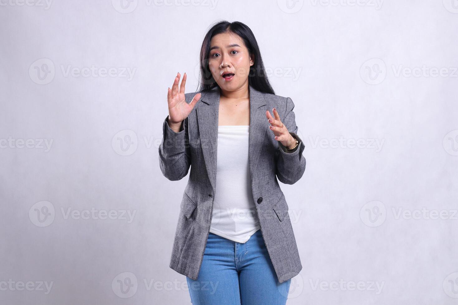 expression of beautiful young girl surprised both arms spread in front of chest wearing grey jacket and jeans standing isolated on white background. for advertising content, fashion, banner, magazine photo