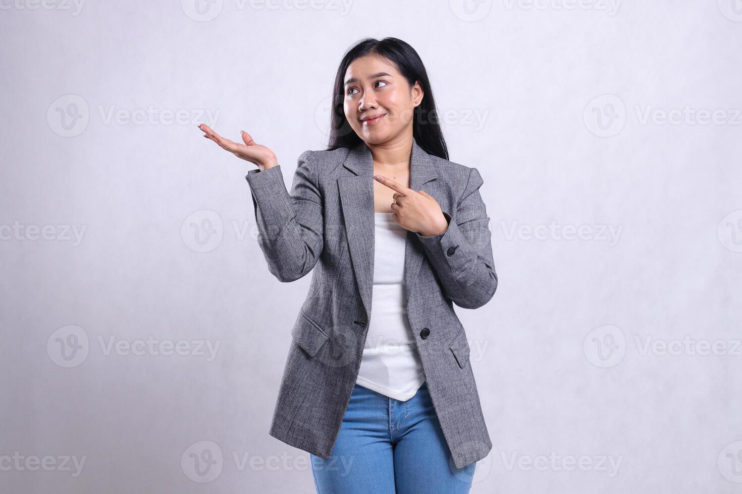 expression of beautiful young woman indonesia smile hand pointing, presenting, look to the right wearing gray suit and jeans standing isolated on white background. for advertising content, magazine photo