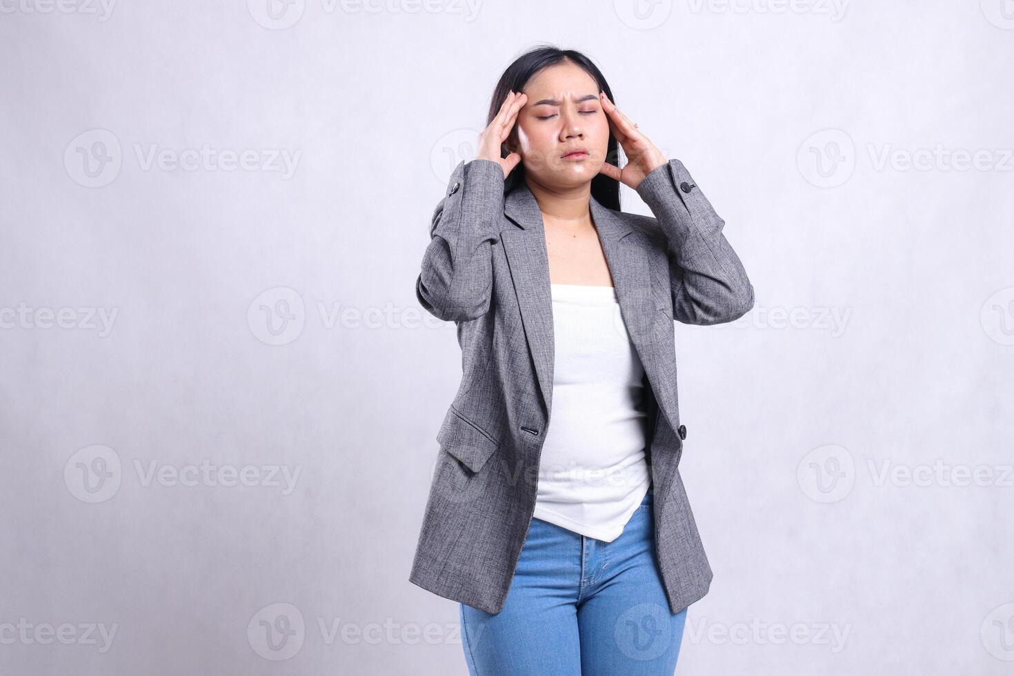 expression of beautiful young office woman asia close eyes dizzy both hands hold head tilted left wearing gray suit standing isolated on white background. for health, medical, commercial, prevention photo