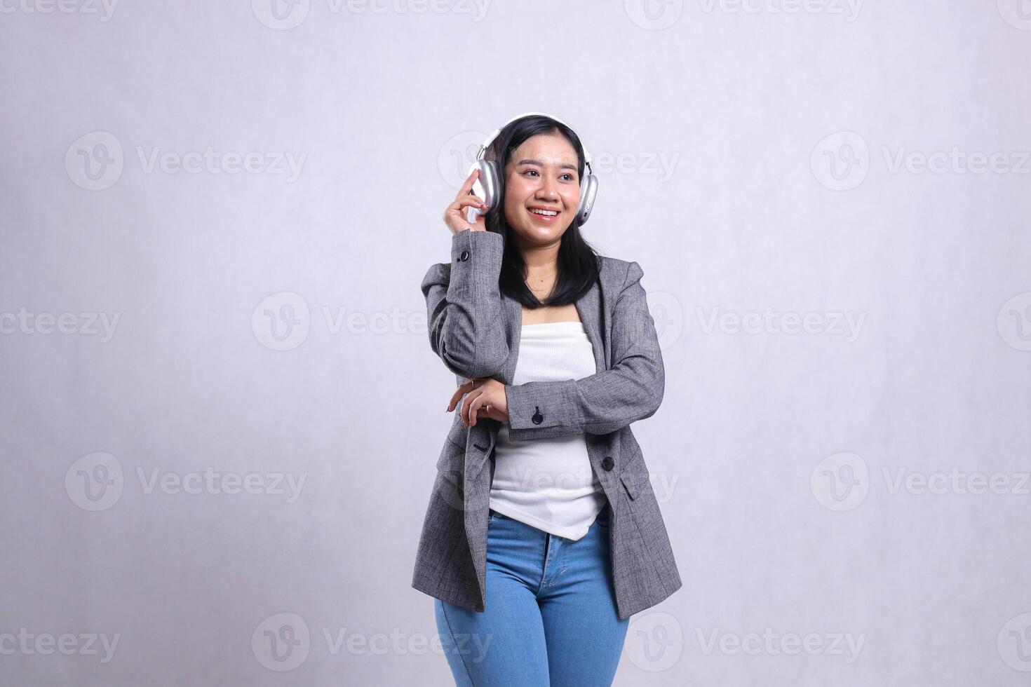 beautiful young office female cheerful candid hugging holding and wearing headphone headset listening to music streaming tone wearing grey suit isolated on white background. lifestyle, advertising photo