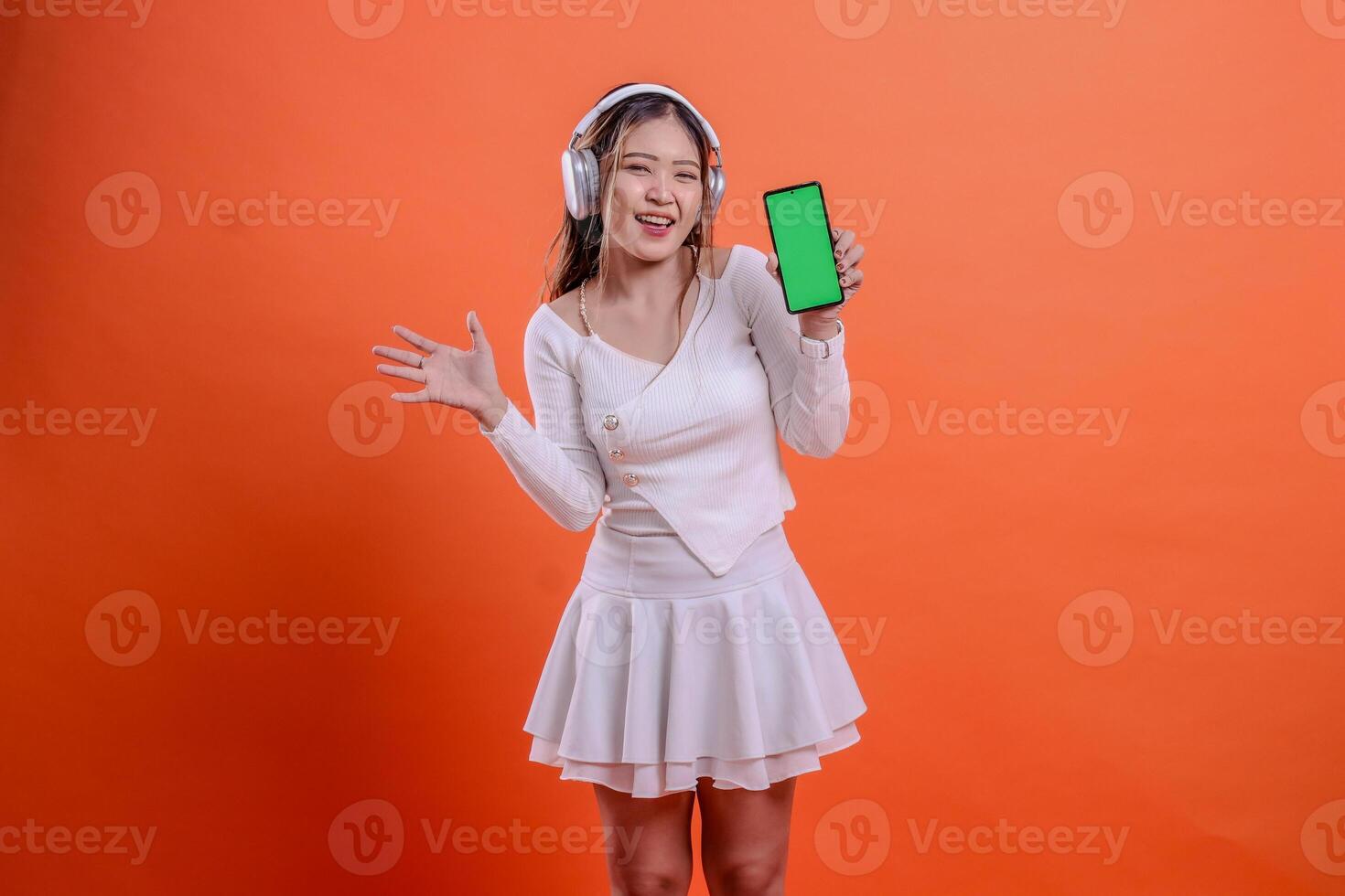gesture cheerful young ladies woman in white sweater wearing earphone headphone, holding mobile phone screen, cellphone green screen while waving sideways. for entertainment, lifestyle, business photo