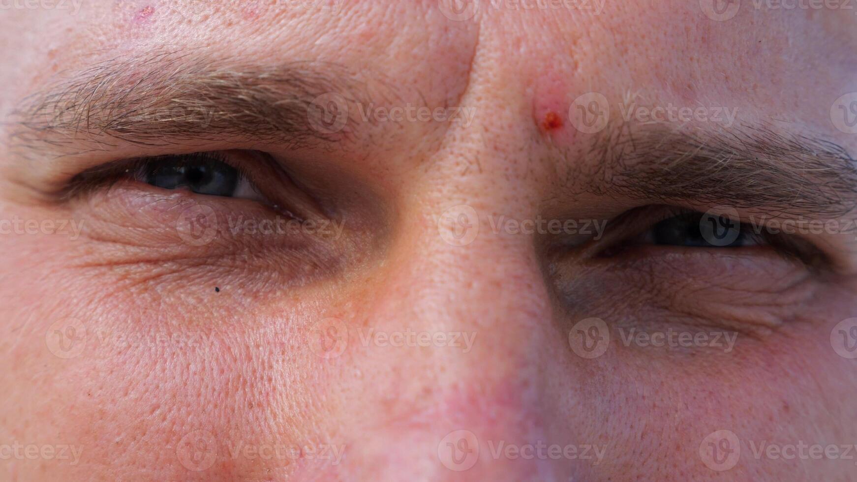 Close up to upset male face looking into camera with a disappointing sight. Upset facial expression of man with blue eyes. Unhappy gaze of despairing young guy. Slow motion photo