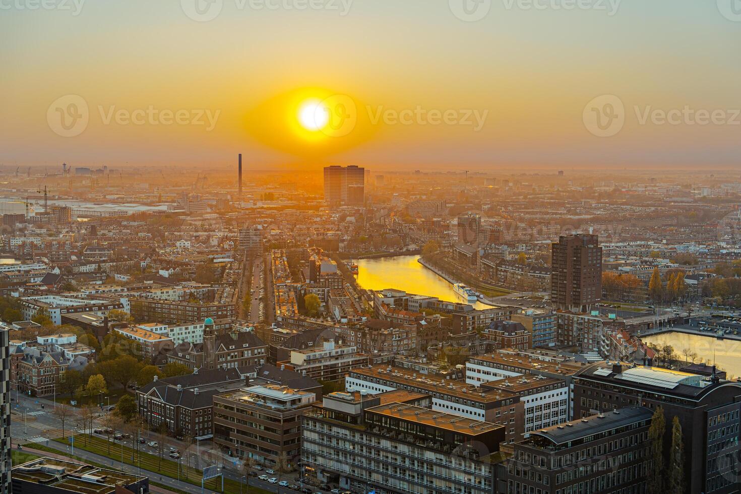 A stunning cityscape at sunset. The warm glow of the setting sun casts a golden hue over the buildings and streets below. A river flows through the city, adding to its beauty. photo