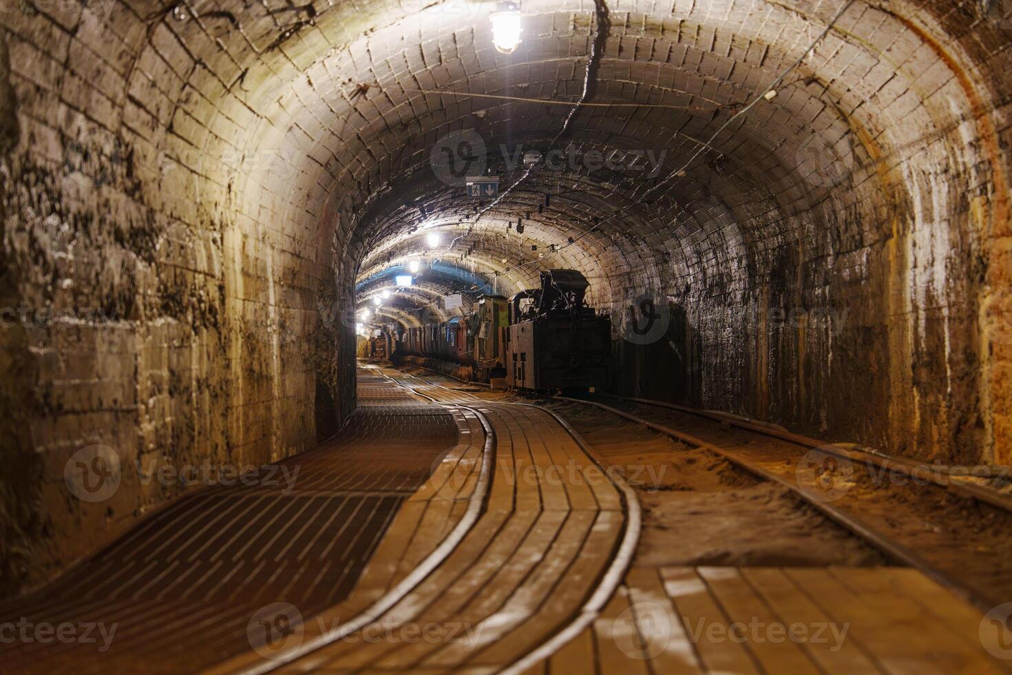 An old abandoned mine tunnel features rusty metal rails and rough stone walls, creating a dark and spooky atmosphere that evokes a sense of history and mystery. photo